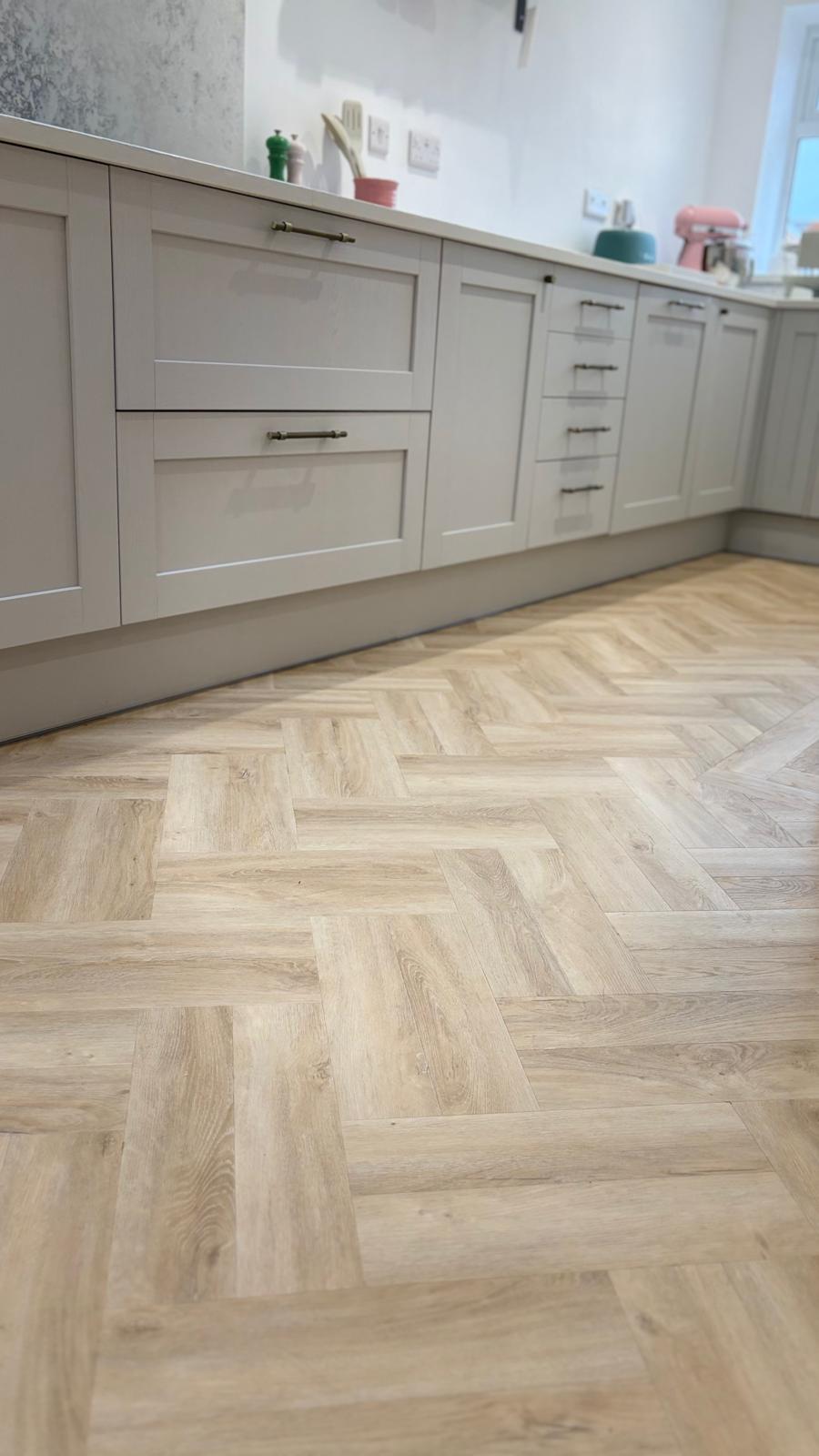 Pale herringbone glue-down LVT fitted beneath painted kitchen cabinetry